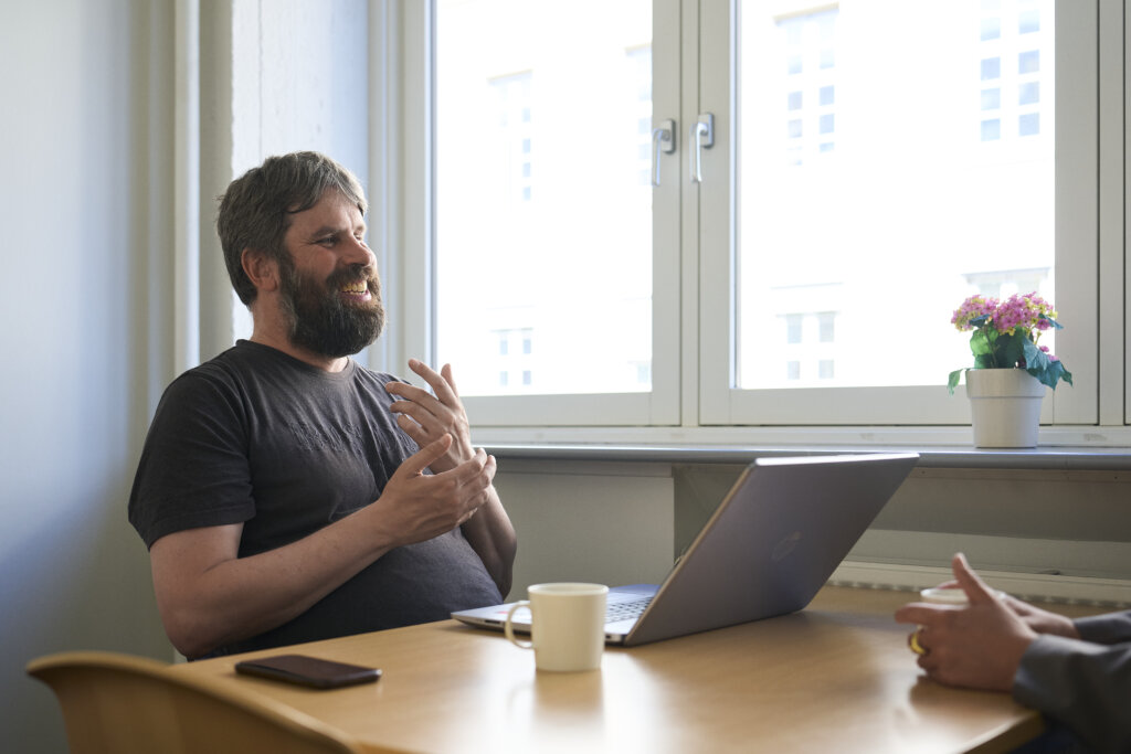 Esben sidder ved et bord med sin computer og griner
