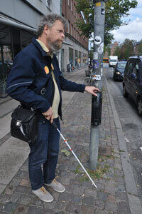 Blind person står ved lydfyr, der med lyd markerer, hvornår det er trygt at gå over.