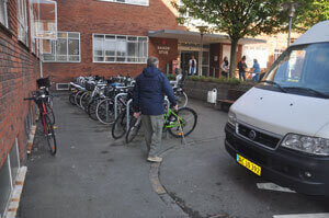 Blind person går langs fortov, mod indgangsparti. Fortovet forsvinder, og den blinde person er ved at gå ind i parkerede cykler.