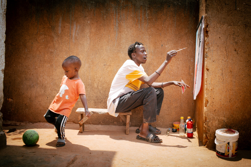 Jean de Dieu maler på sit portræt uden for, mens 3-årige Kyrie sparker til en bold