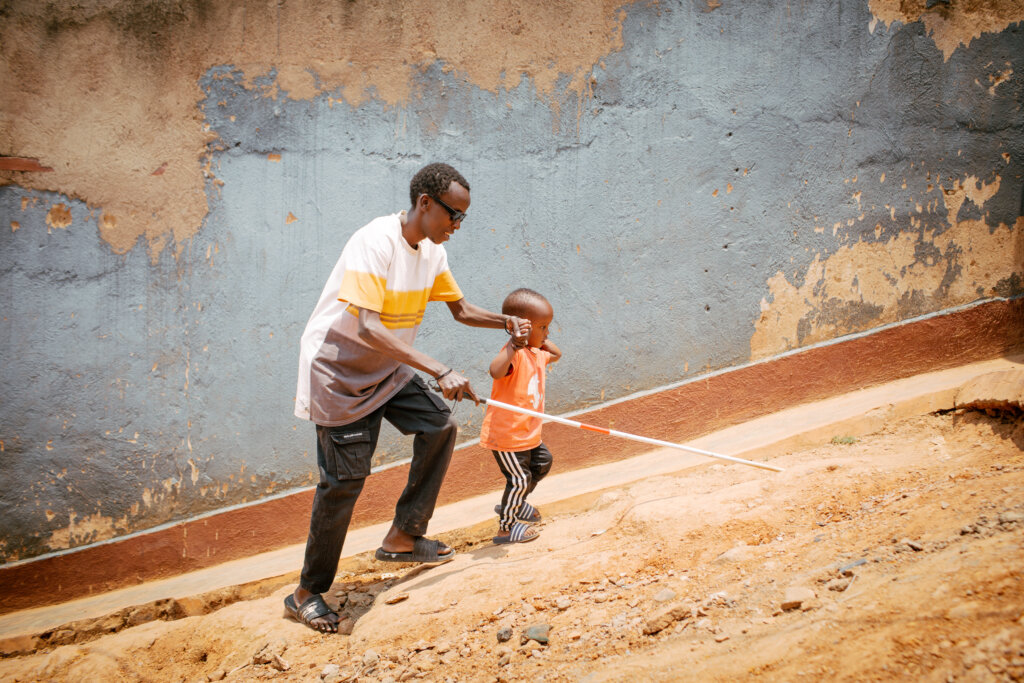 Jean går op af en stejl skrænt med sin blindestok i den ene hånd og sin søn på tre år i en anden hånd