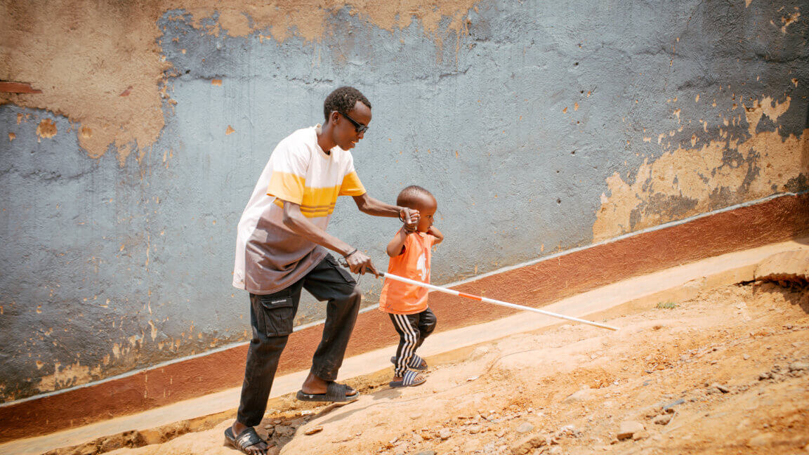 Jean går op af en stejl skrænt med sin blindestok i den ene hånd og sin søn på tre år i en anden hånd