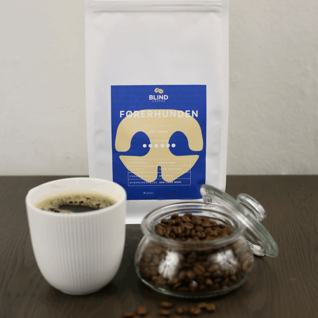 Billedet viser en kop kaffe, en pose med kaffebønner, samt en glas beholder med kaffebønner i, som alt sammen står på et bord