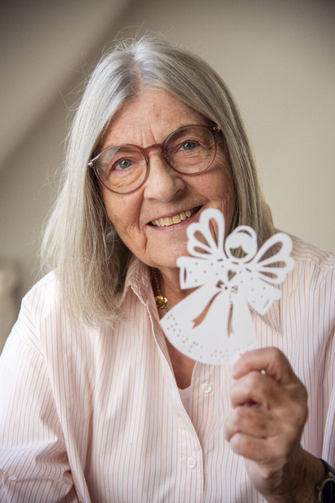 Portræt af smilende Gitte, hvor hun holder en papir juleengel i venstre hånd.