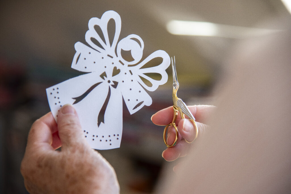Billede af Gittes hænder, hvor hun i højre hånd holder en saks, og i venstre hånd holder en juleengel af papir
