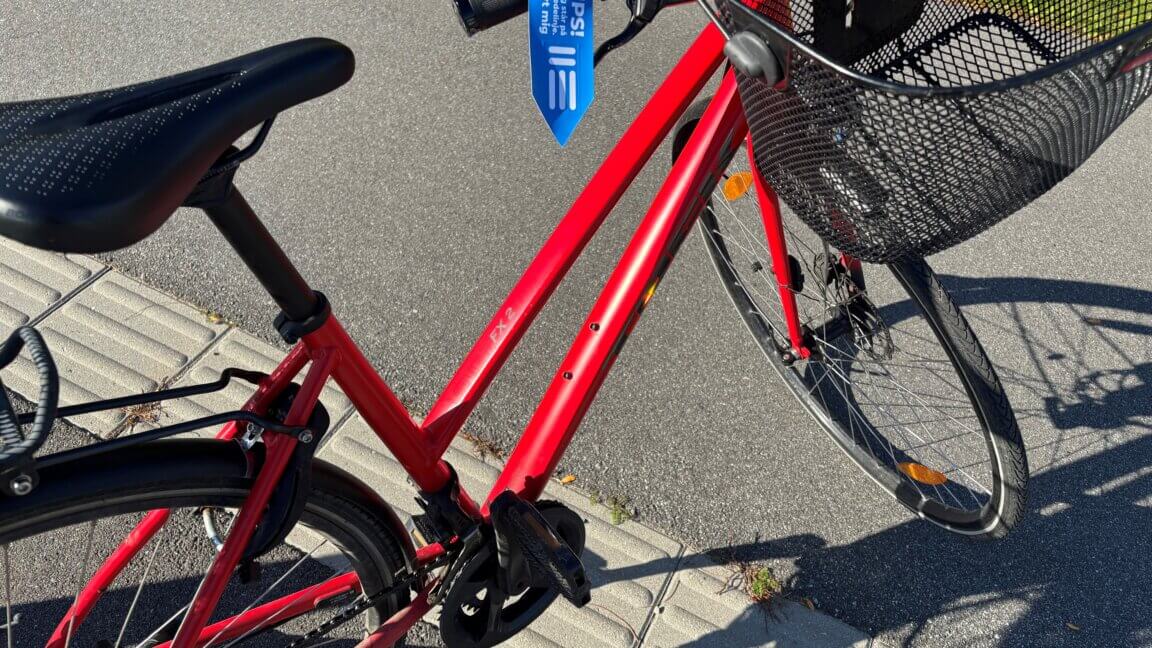En rød cykel spærrer en ledelinje. På stativet er det blå mærkat med teksten: UPS! Jeg står på en ledelinje. Flyt mig