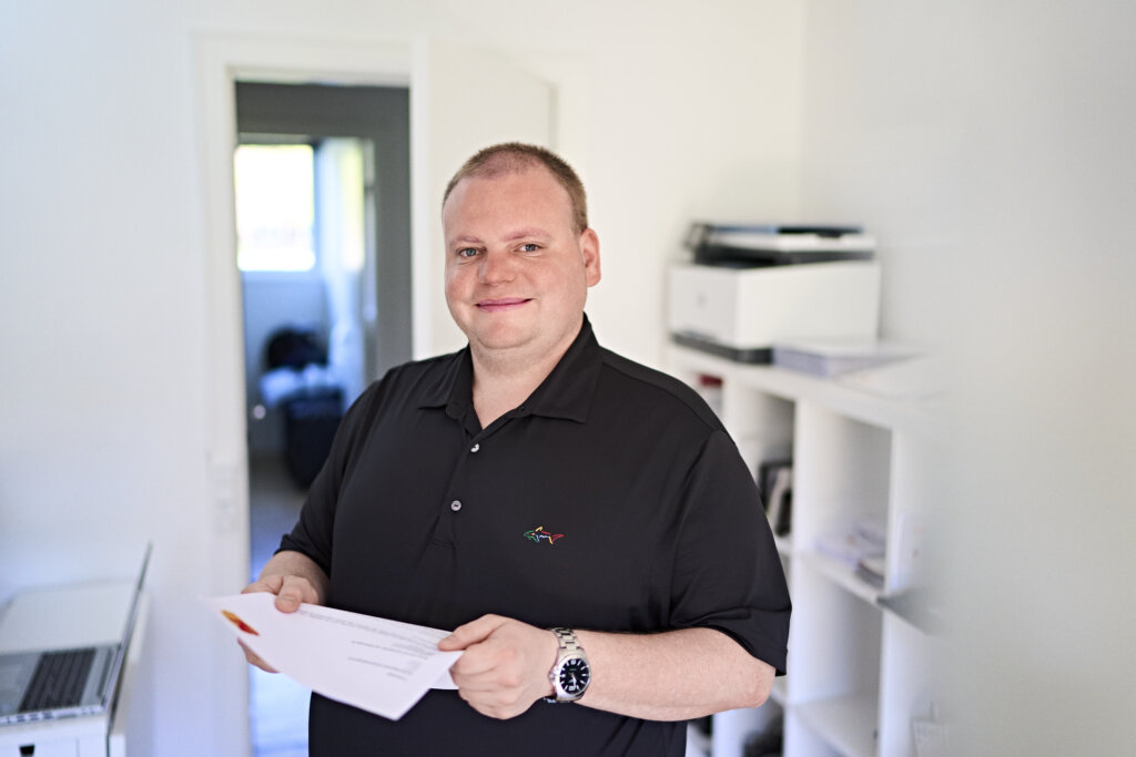 Portræt af Lasse som står med en stak papirer