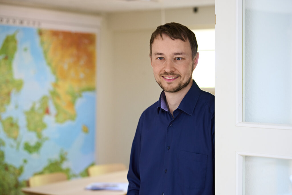 Portr&aelig;t af s&oslash;ren, det st&aring;r p&aring; hans kontor. I baggrunden ser man noget af et verdenskort h&aelig;nge p&aring; v&aelig;ggen. 