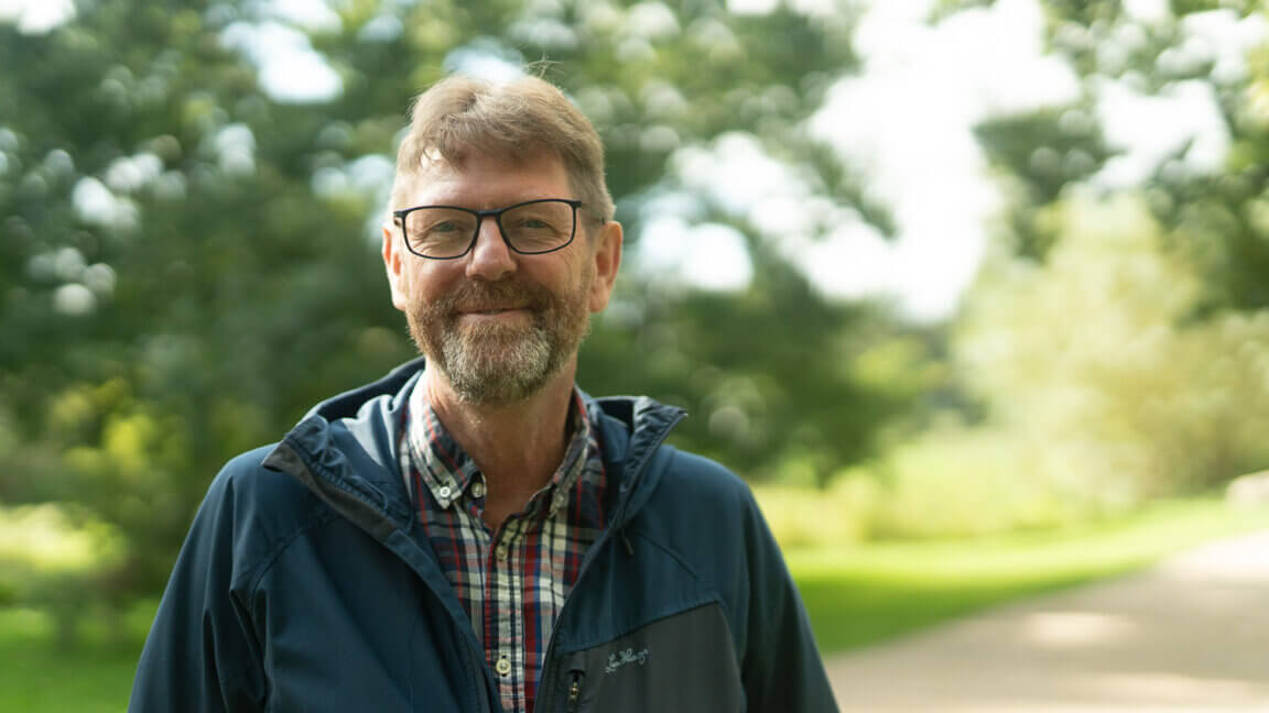 Portræt af Henrik From, der står ud i det grønne omringet af træer og buske.