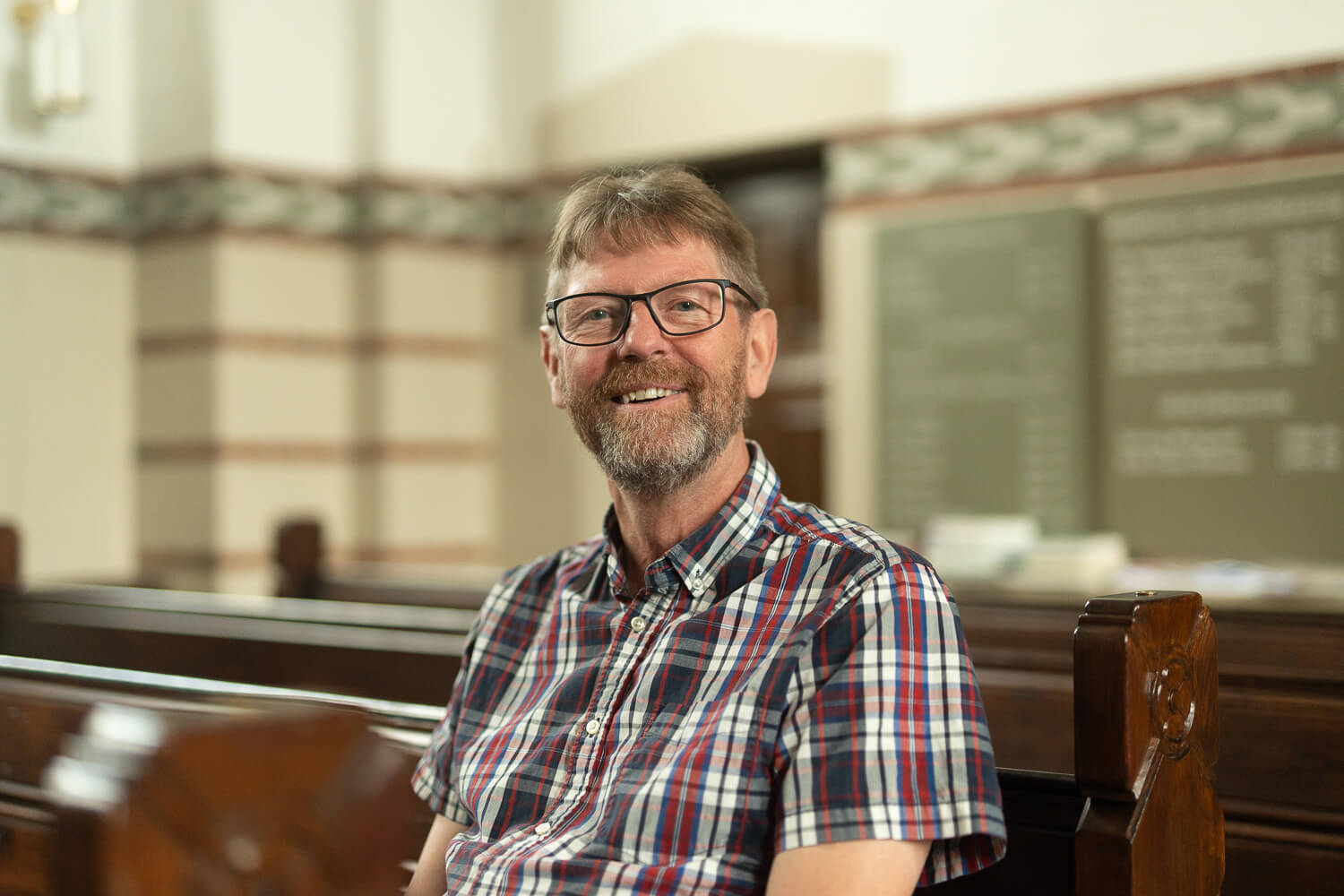 Portræt af Henrik From. Henrik sidder i en kirke, og smiler ind i kameraet.