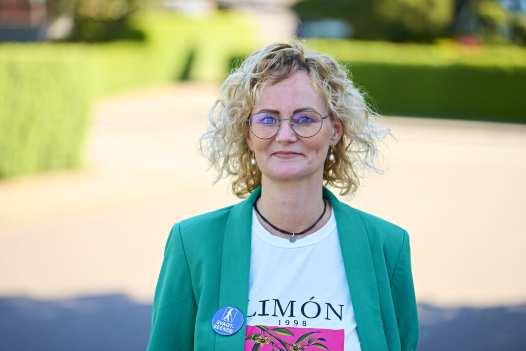 Portr&aelig;t af Rikke uden for med badge, hvor der st&aring;r svagtseende