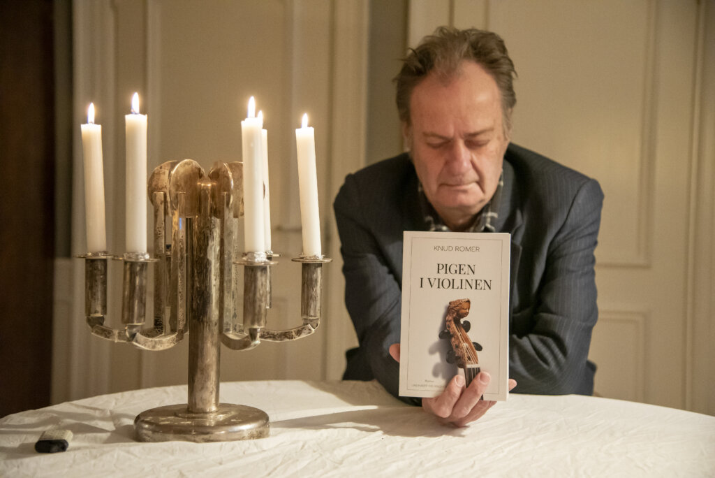 Knud Romer holder sin egen bog frem Pigen i violinen. Han har lukkede &oslash;jne og foran ham st&aring;r en lysestage med t&aelig;ndt lys