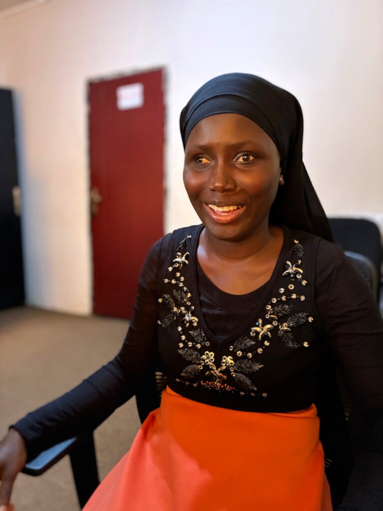 Mariatou sidder smilende med t&oslash;rkl&aelig;de p&aring; hovedet og paliet tr&oslash;je