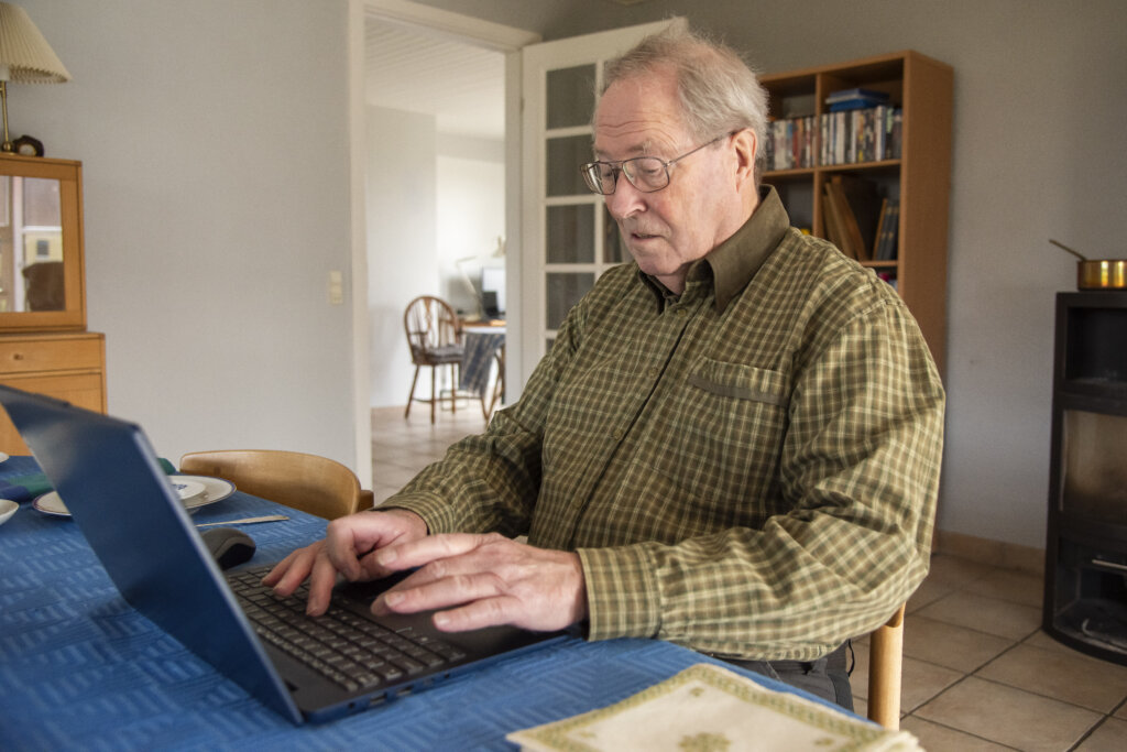 Michael sidder ved spisebordet og skriver p&aring; computer
