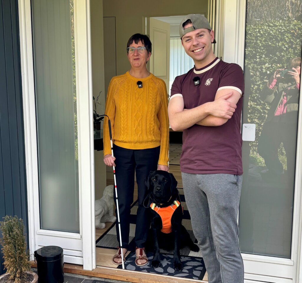 Lene og Morten står i døråbningen med førerhunden Aston, en sort labrador