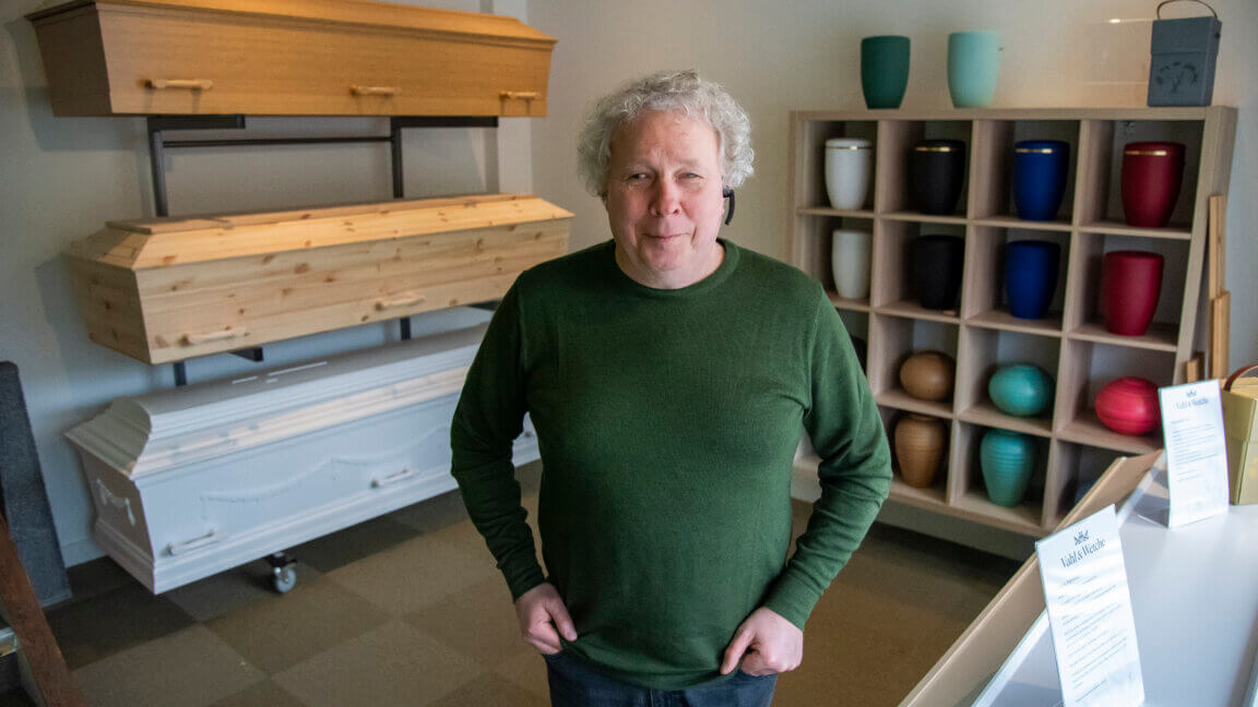 Thomas står i sin begravelsesforretning. I baggrunden står der urner og kister hænger til udstilling