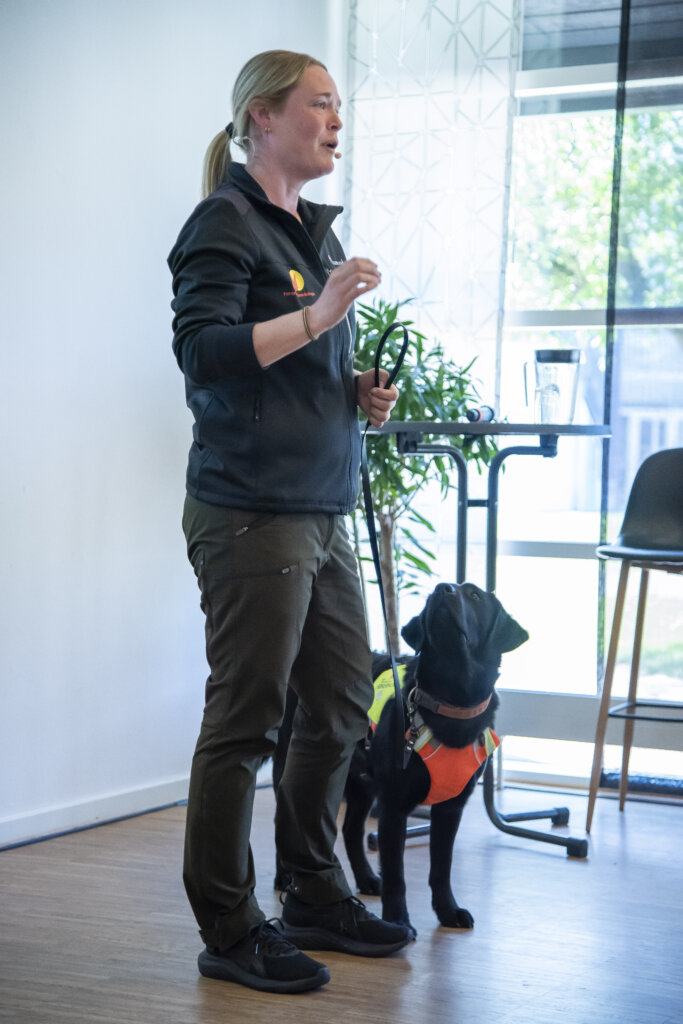 F&oslash;rerhundeinstrukt&oslash;r Tine st&aring;r med f&oslash;rerhunden Visti, en sort labrador med f&oslash;rerhundeb&oslash;jle p&aring;