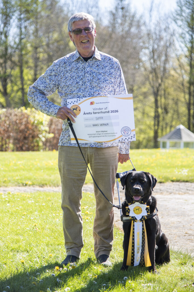 Hans Verner holder et gavekort. Ved siden af ham sidder f&oslash;rerhunden Siffi, en sort labrador, som b&aelig;rer en roset, hvor der st&aring;r &Aring;rets f&oslash;rerhund 2026