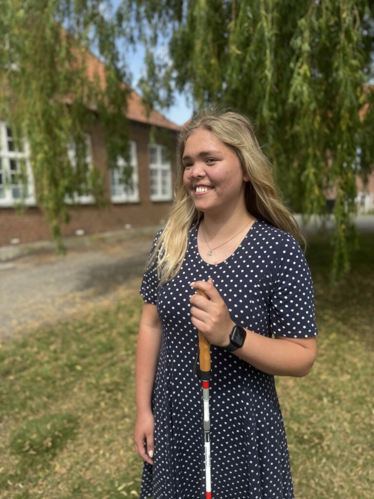 Sarah st&aring;r smilende med sin blindestok uden for