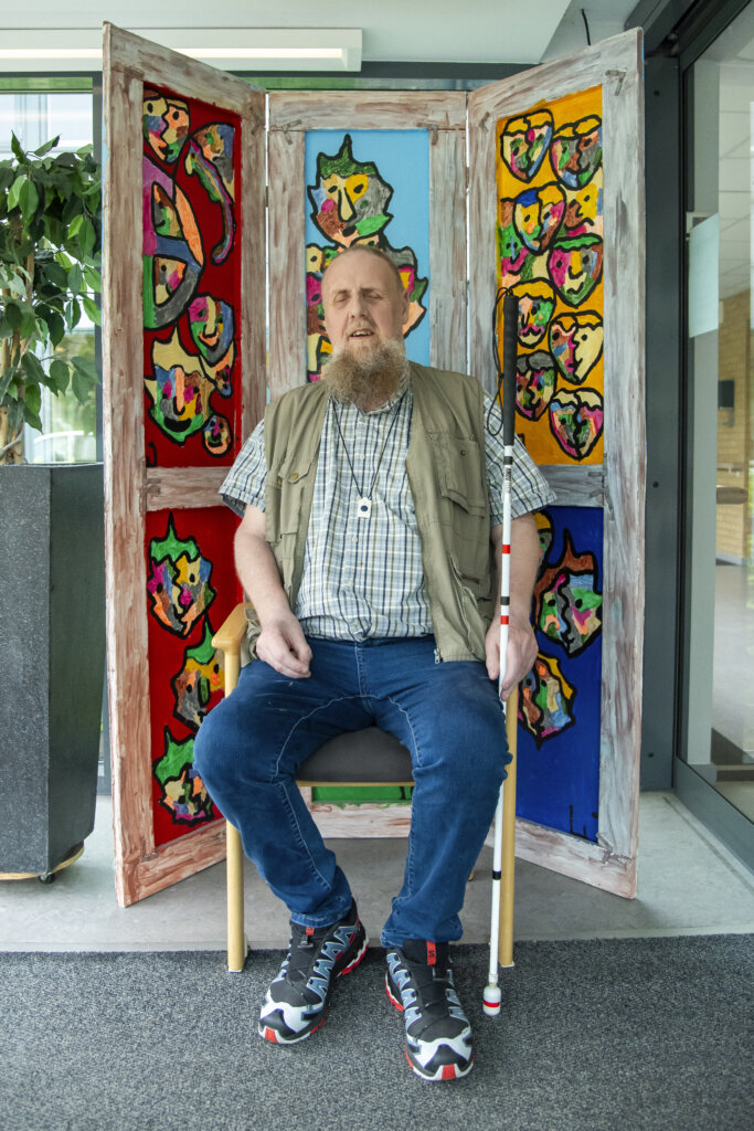 Lars sidder foran et stort maleri, han selv har lavet med varme farver og forskellige ansigter