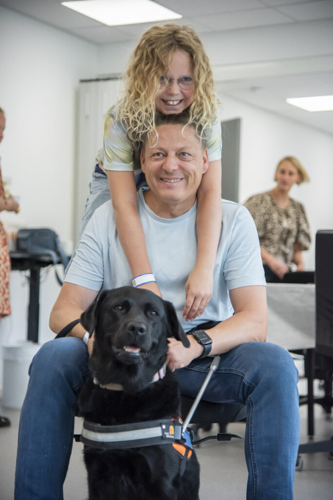 Mira h&aelig;nger p&aring; sin far Kenneth, der holder f&oslash;rerhunden Astrid, sort labrador i f&oslash;rerhundeb&oslash;jle