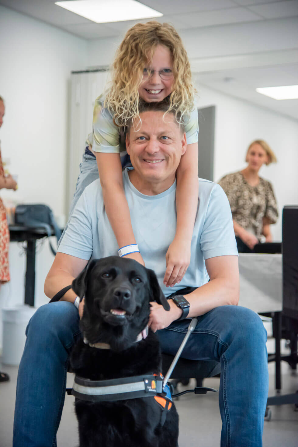 Mira hænger på sin far Kenneth, der holder førerhunden Astrid, sort labrador i førerhundebøjle