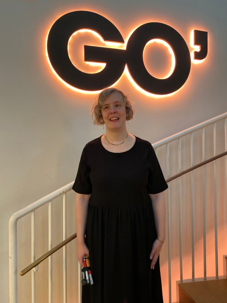 Anne Sofie st&aring;r p&aring; trappen til Go' morgen Danmarks studie. Bag hende er et stort lysende logo, hvor der st&aring;r: GO