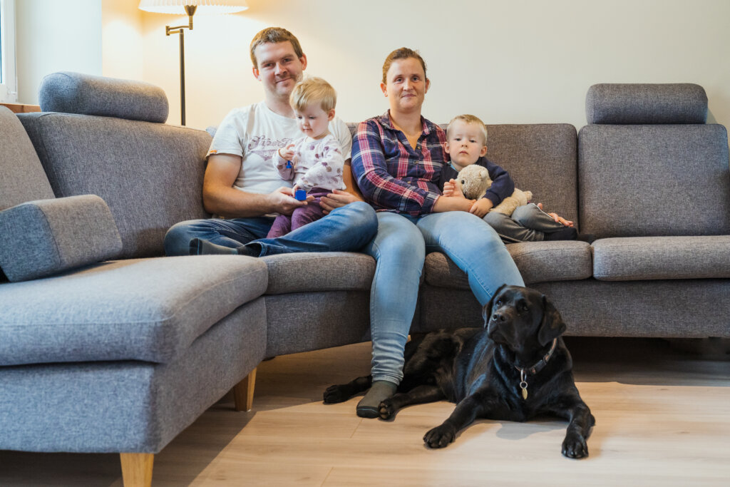 Ann-Sofie fra Blind mors dagbog sidder i en sofa med sin familie - en mand og to børn. Foran dem ligger hendes førerhund, en sort labrador