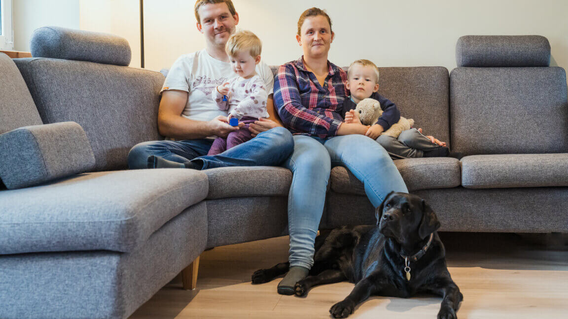 Ann-Sofie fra Blind mors dagbog sidder i en sofa med sin familie - en mand og to børn. Foran dem ligger hendes førerhund, en sort labrador