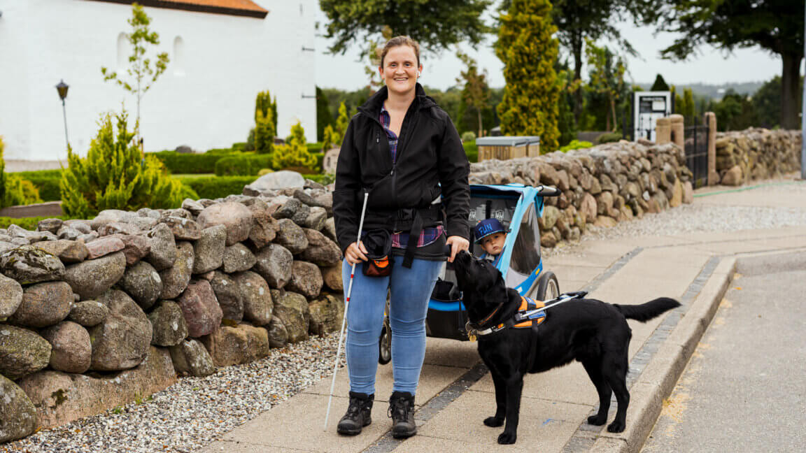 Ann-Sofie og sin førerhund står foran cykelanhængeren som Ann-Sofie anvender i dagligdagen fx når der skal afleveres børn.